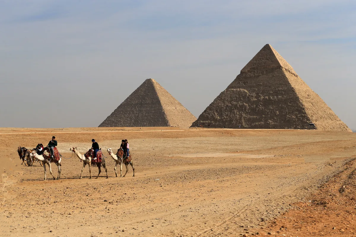 Camel riders crossing the desert in front of the Giza pyramids