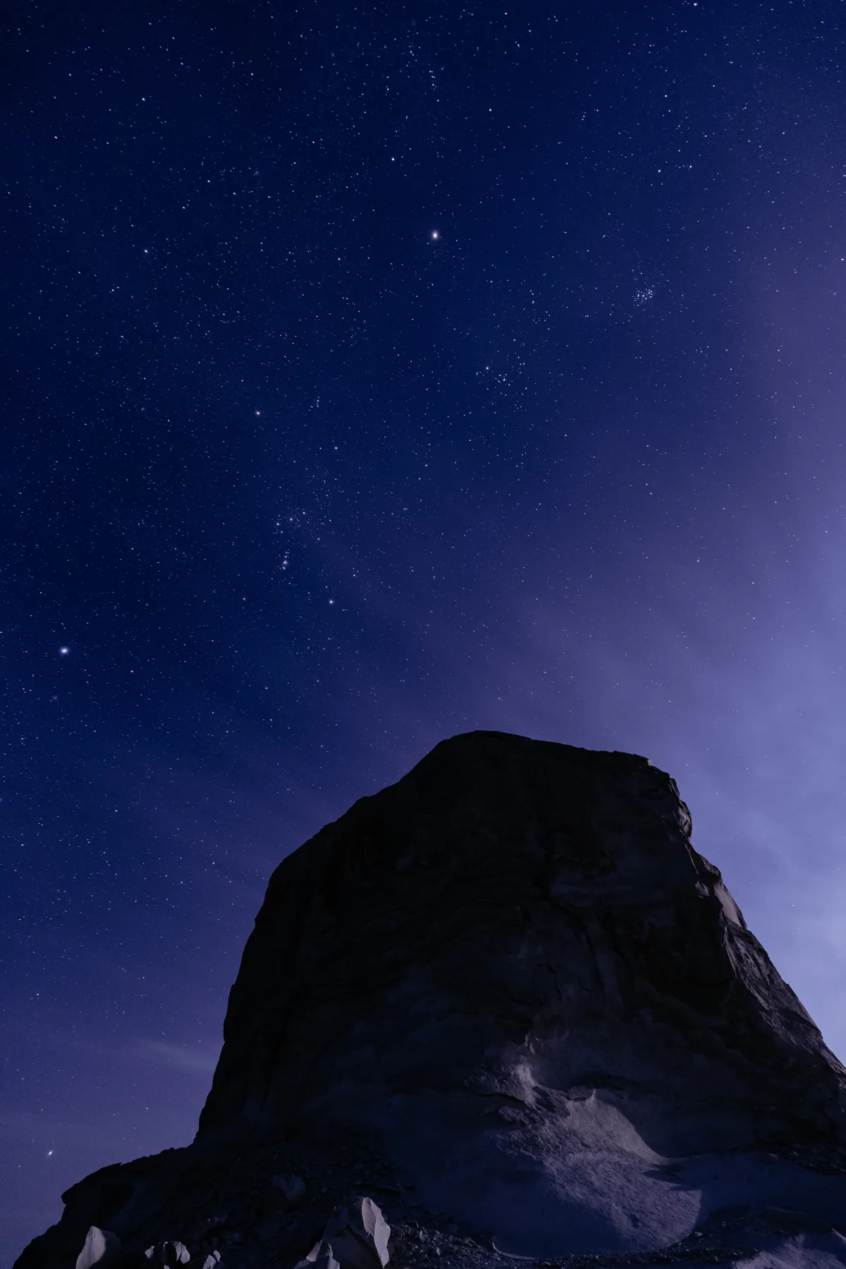 Star-filled night sky above a dark desert rock formation