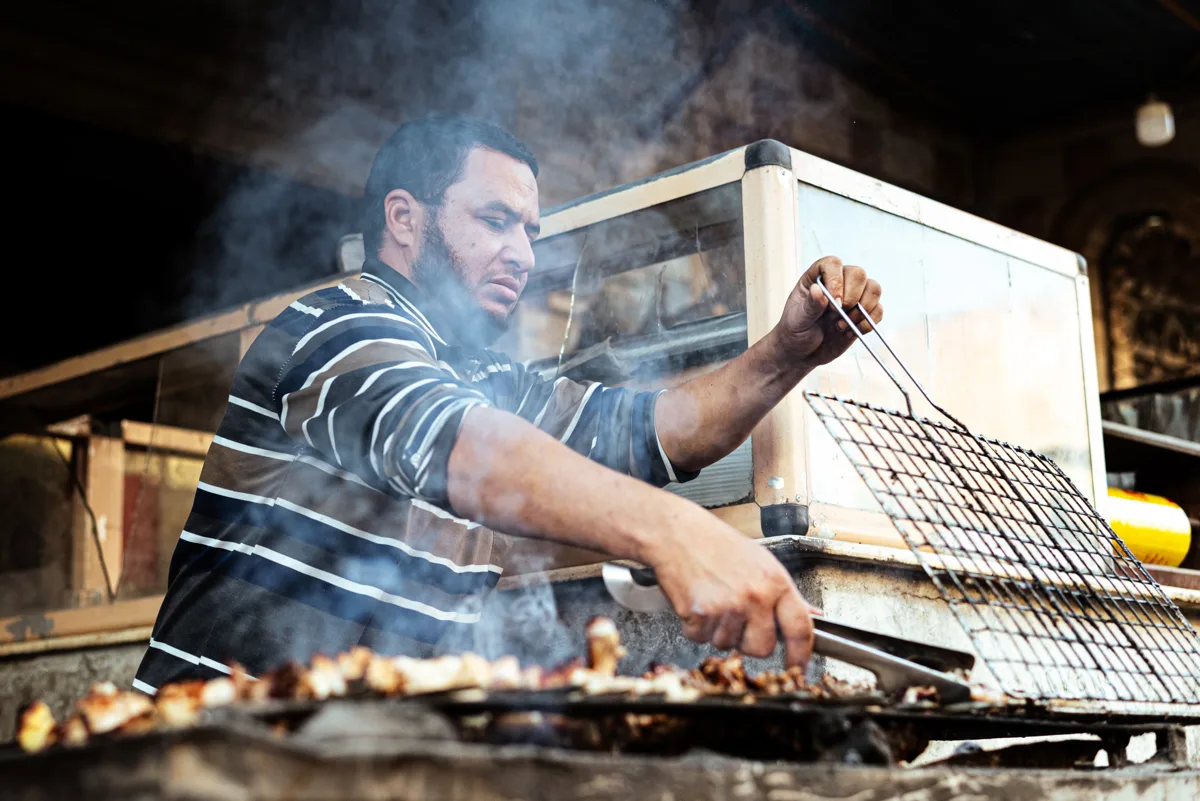 Street-food cook grilling meat over glowing charcoal